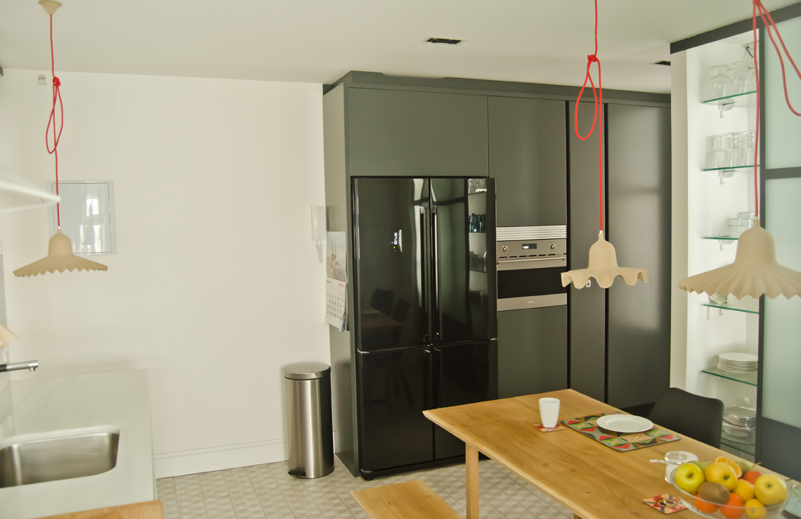 El programa de la cocina se completa con un bloque de armarios que incluye frigorífico, horno y despensa en un espacio que da paso al dormitorio de servicios-invitados-almacén con aseo propio que también da servicio a la cocina